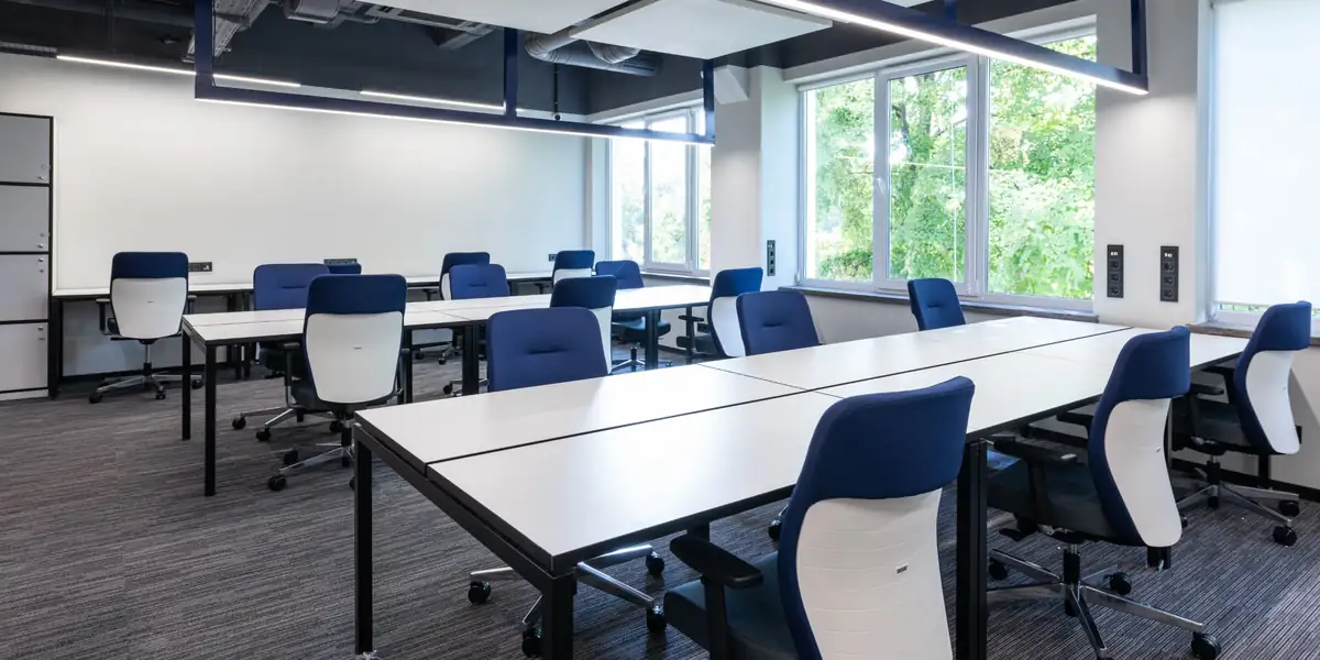 Blue and white office chairs at white desks in a bright office with large windows