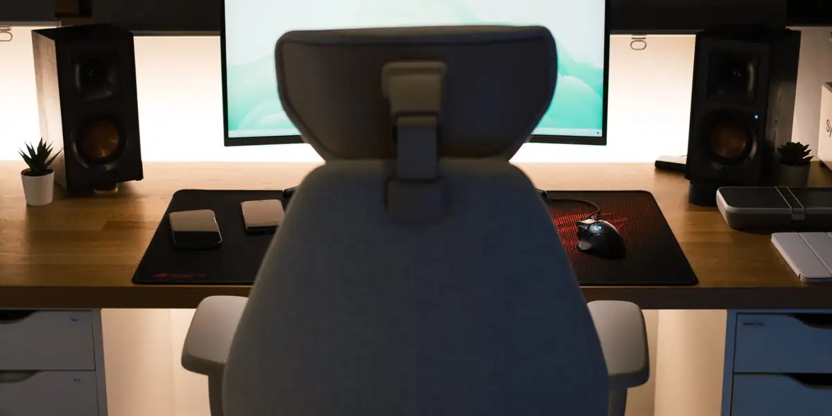 Grey office chair with a headrest facing a monitor at a softly lit desk