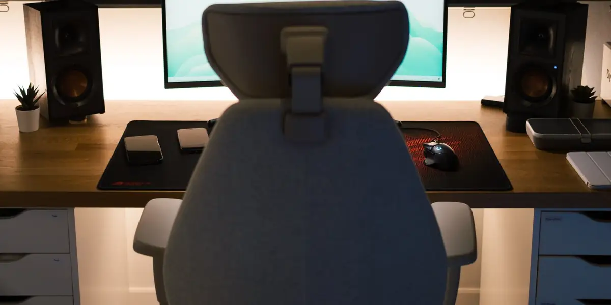 Gray fabric office chair with a headrest facing a monitor and speakers on a wooden desk