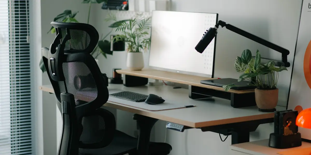 Black mesh ergonomic office chair with a headrest at a height-adjustable desk with a monitor and plants