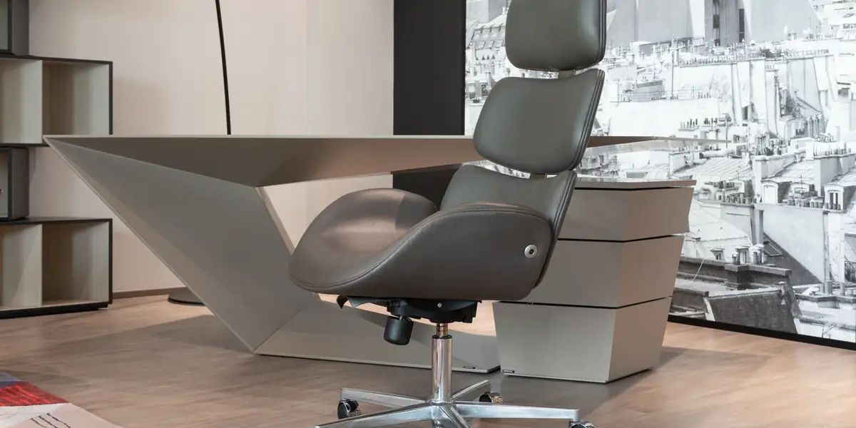 Gray leather executive office chair with a headrest beside a sculptural desk