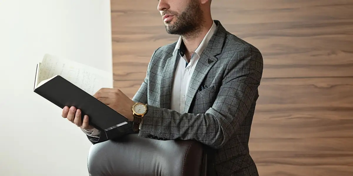 Man reading a notebook while leaning on a brown leather executive office chair