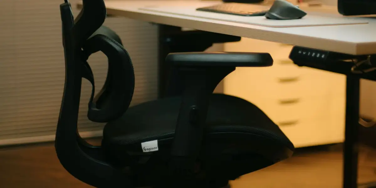 Black mesh office chair with a headrest and adjustable arms at a desk in warm evening light
