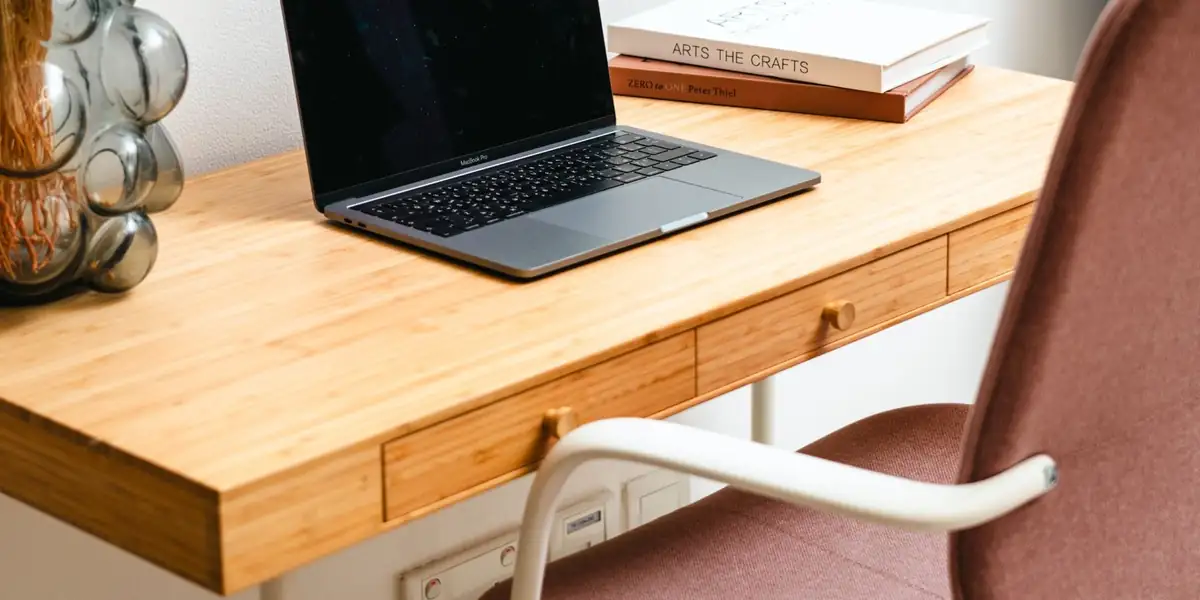 Pink upholstered office chair at a bamboo desk with a laptop and books