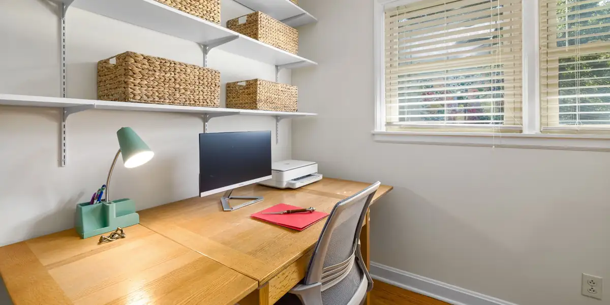Compact home office with a wooden desk, monitor, mesh chair and storage shelves