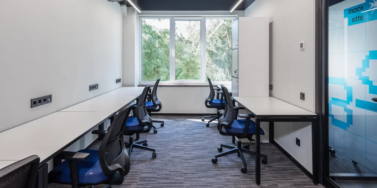 Mesh-back task chairs with blue seats at white desks in a small office with a window