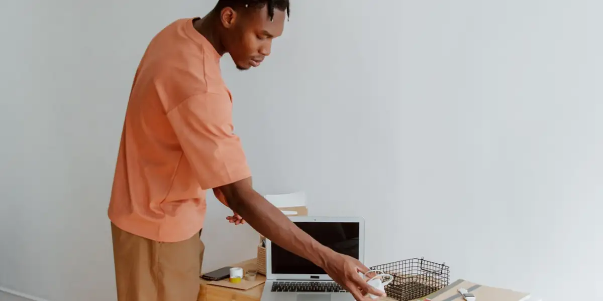 Man standing at a small wooden desk with a white chair and a laptop