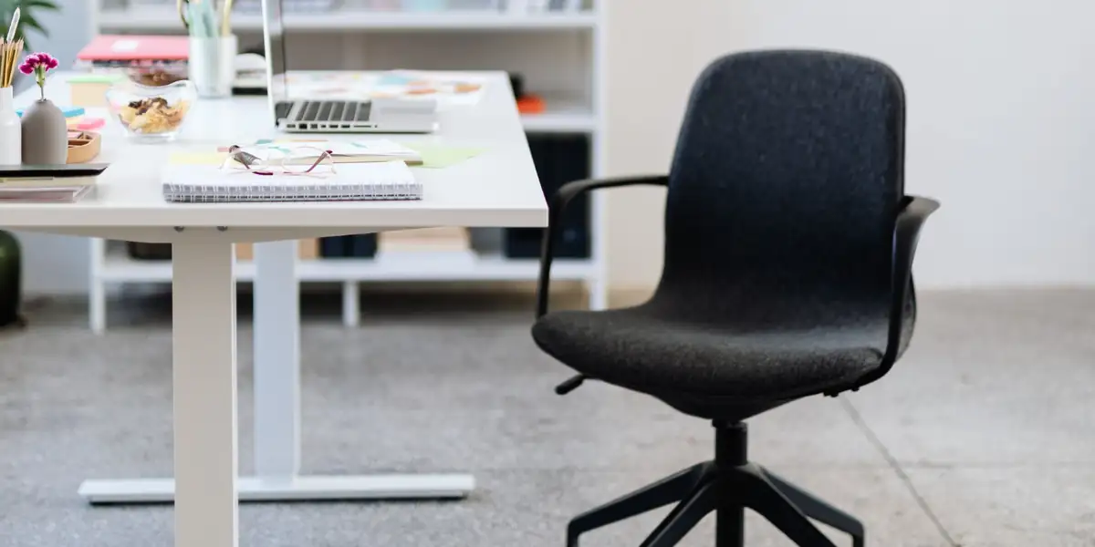 Black upholstered swivel chair beside a white desk with a laptop and plants
