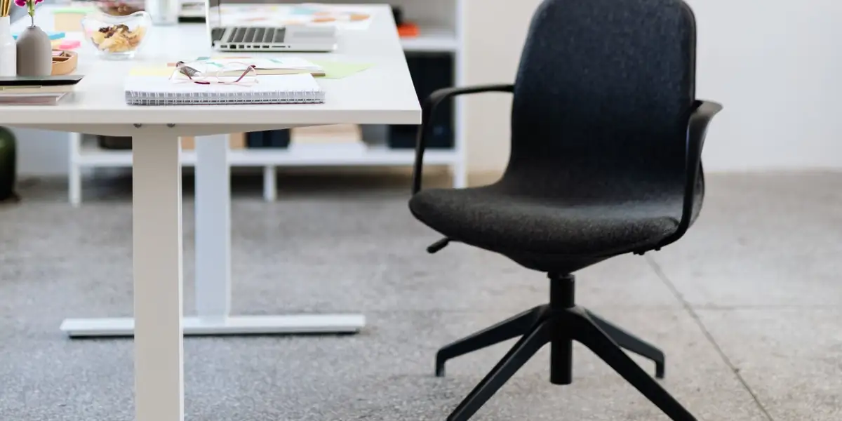 Black upholstered swivel chair beside a white height-adjustable desk with a laptop