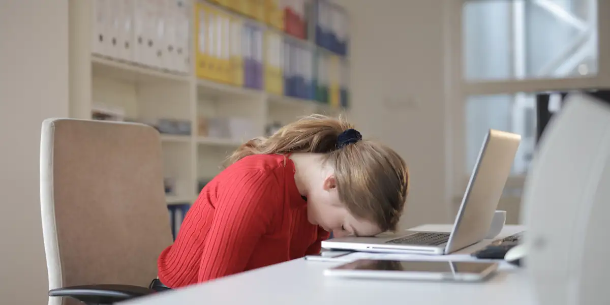Woman resting her head on a laptop while sitting in an office chair at a white desk