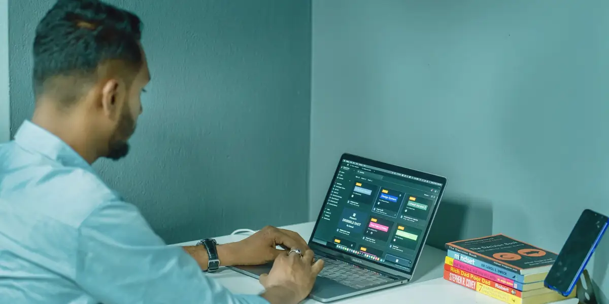 Man in a blue shirt sitting upright and typing on a laptop at a white desk