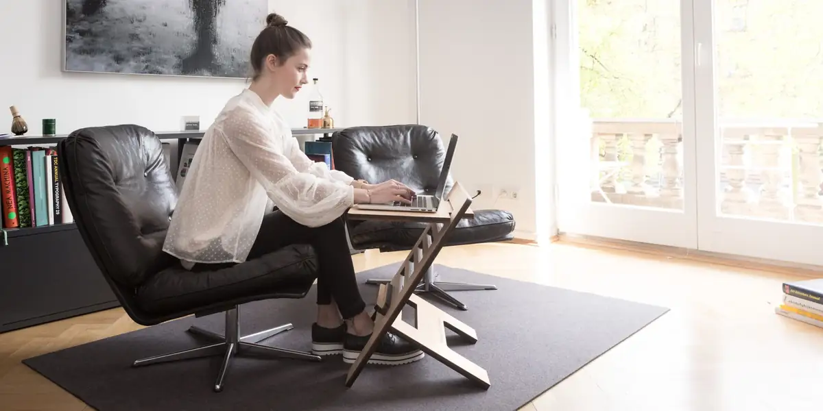 Woman typing on a laptop on a stand while seated in a leather lounge chair at home