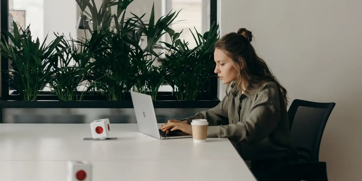 Woman typing on a laptop at a long white desk in a mesh office chair in a bright office